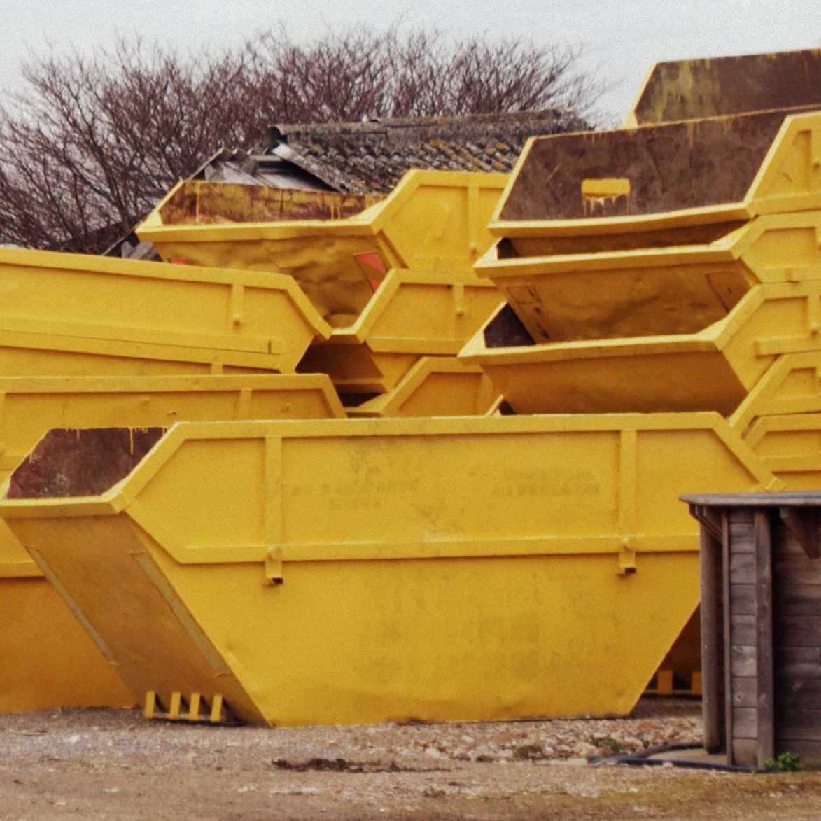 several yellow skips packed on top of each other in a waste field.