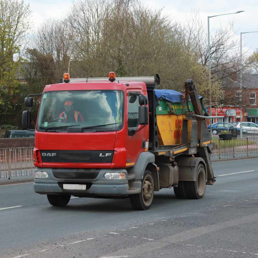 A red skip hire truck driving through a street in nottingham.